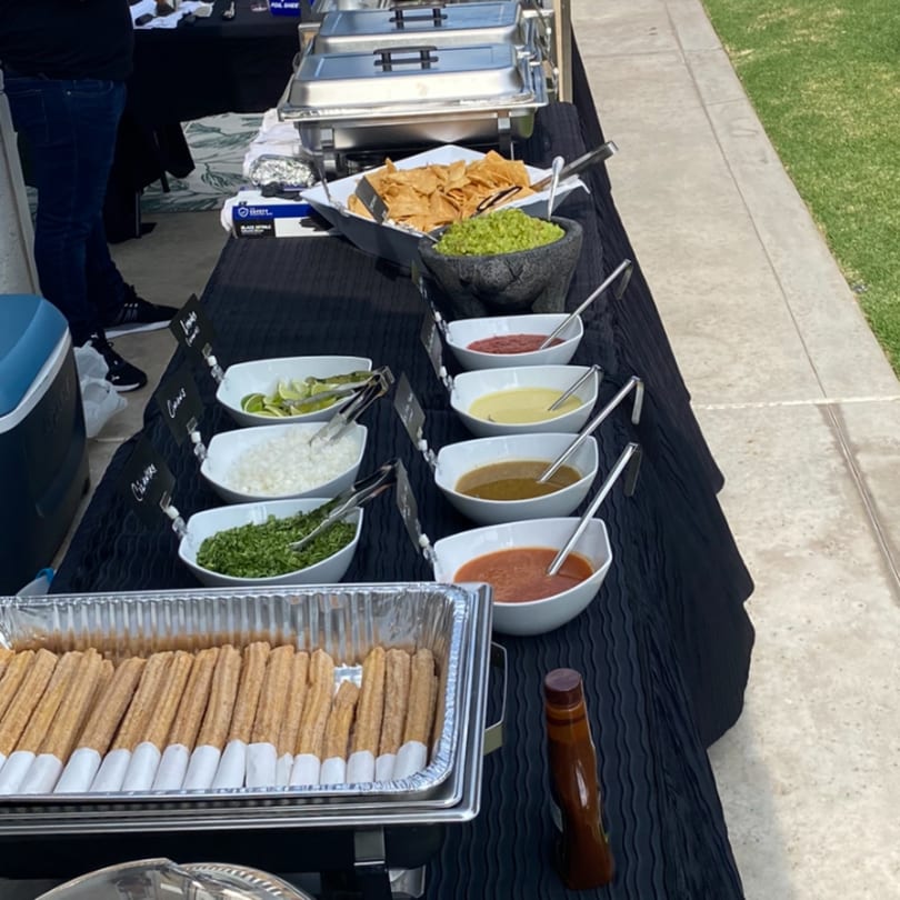 A Bandeño Mexican Food catering spread with churros, chips, guacamole, and various salsas on a black-draped table.