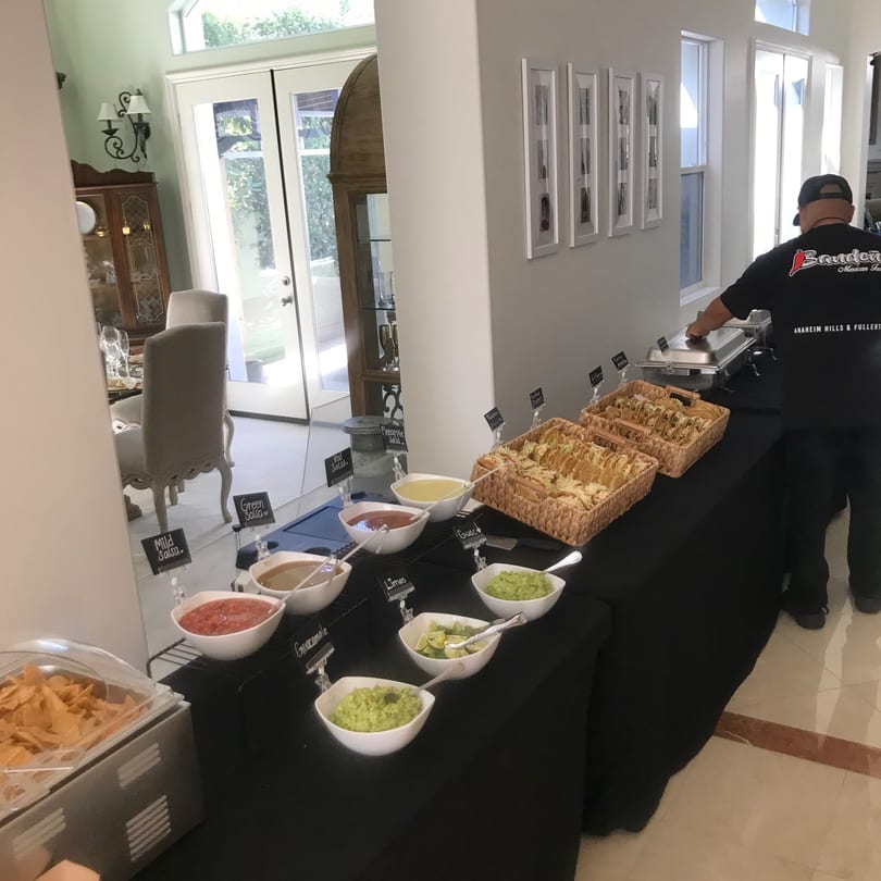 A Bandeño Mexican Food employee sets up a buffet with tacos, chips, guacamole, and various salsas.