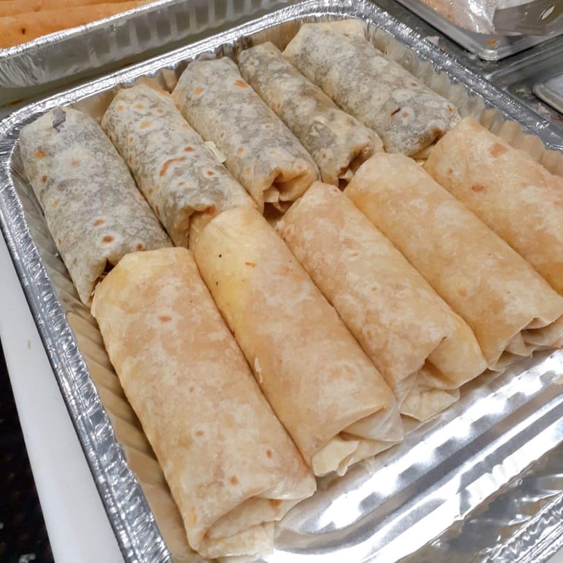 Rows of Bandeño Mexican Food burritos in a foil tray, some lighter, some darker.
