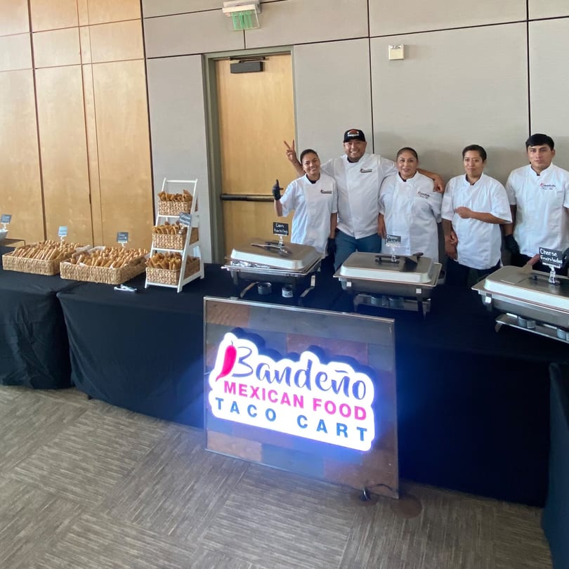 Bandeño Mexican Food staff standing behind a catering table with food warmers and taquitos.
