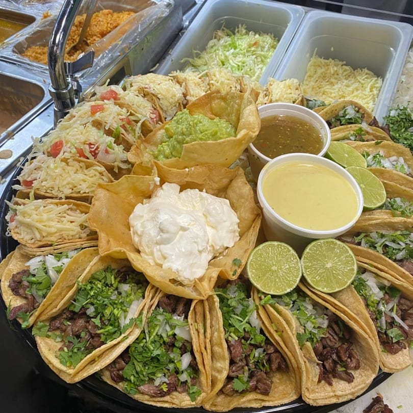 A large platter of Bandeño Mexican Food tacos, with guacamole, sour cream, and sauces.