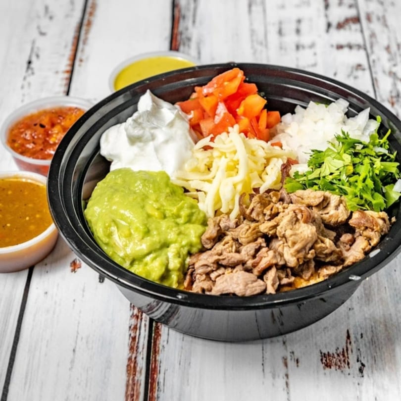 A Bandeño Mexican Food bowl with steak, guacamole, sour cream, cheese, tomatoes, onions, and cilantro.
