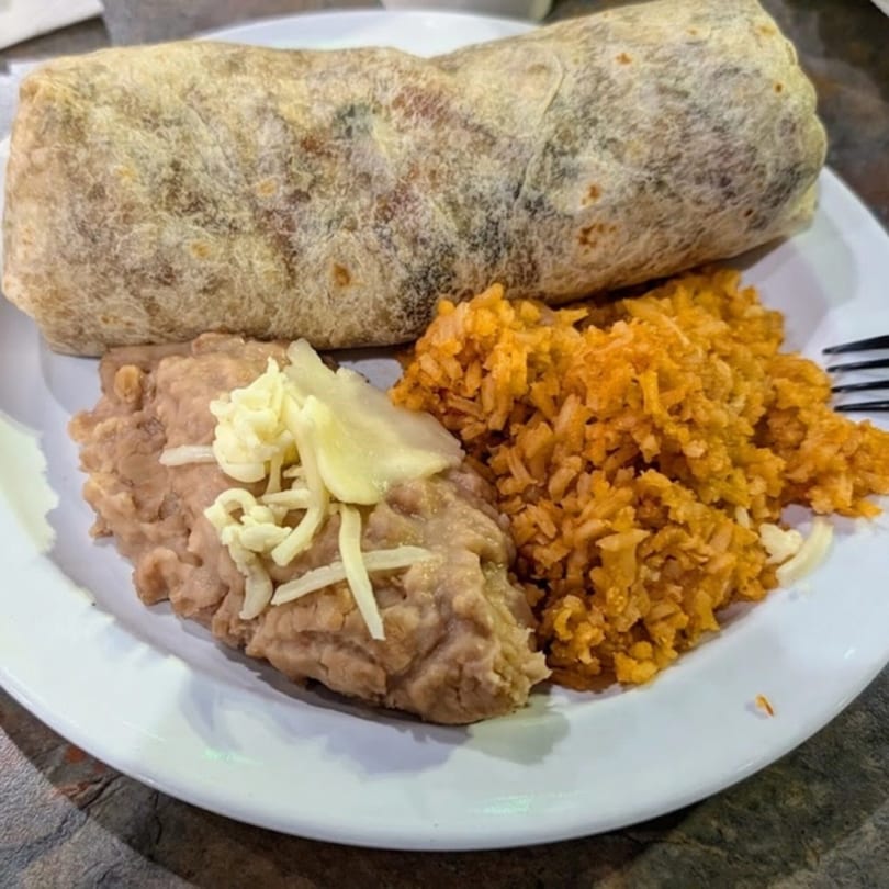 A Bandeño Mexican Food burrito, refried beans with cheese, and orange rice on a white plate.