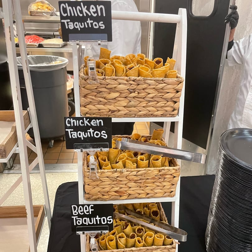 Three baskets of Bandeño Mexican Food taquitos, chicken and beef, on a white display stand.